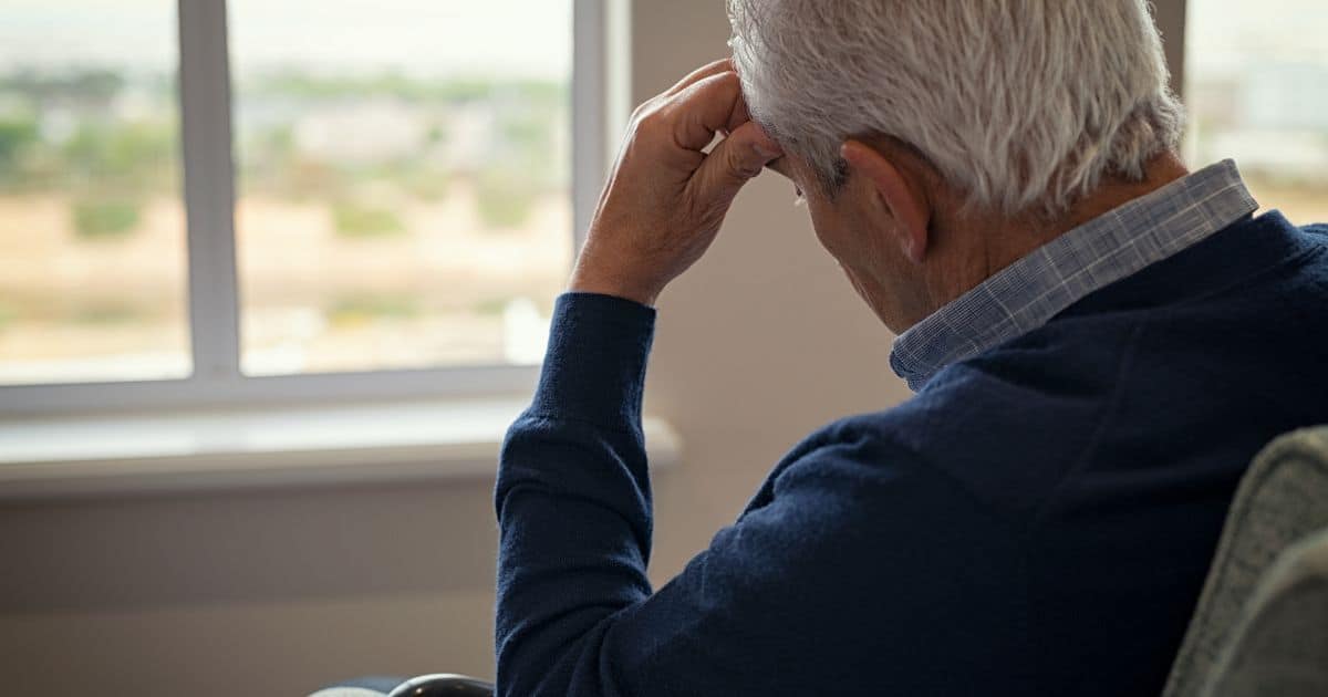older adult with hand on head looking out the window